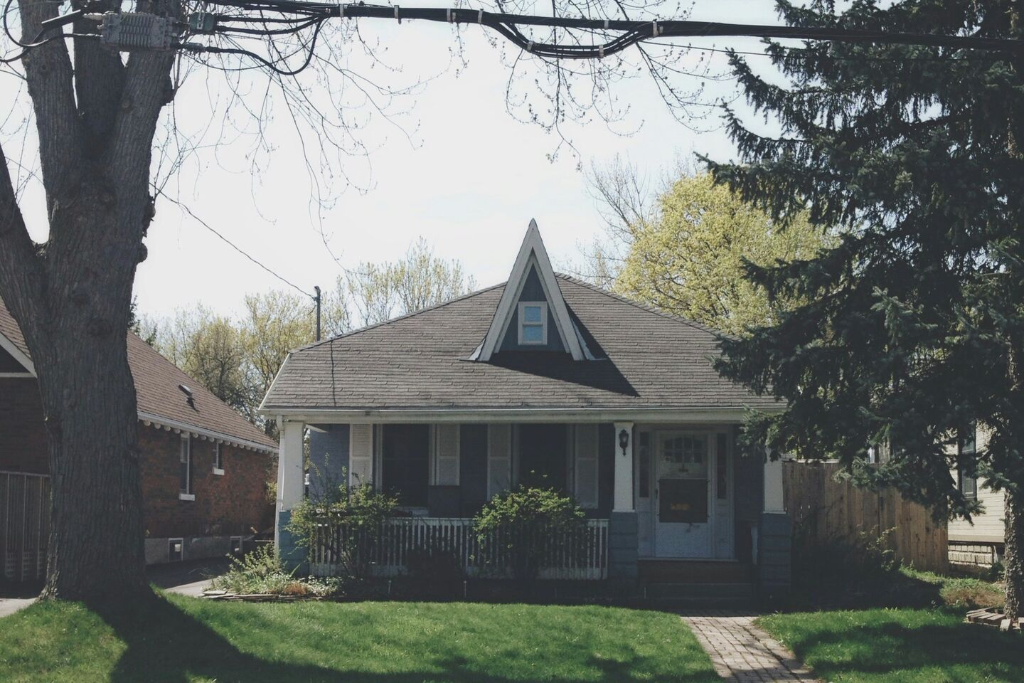 Older bungalow with a front porch, a large tree and a lawn
