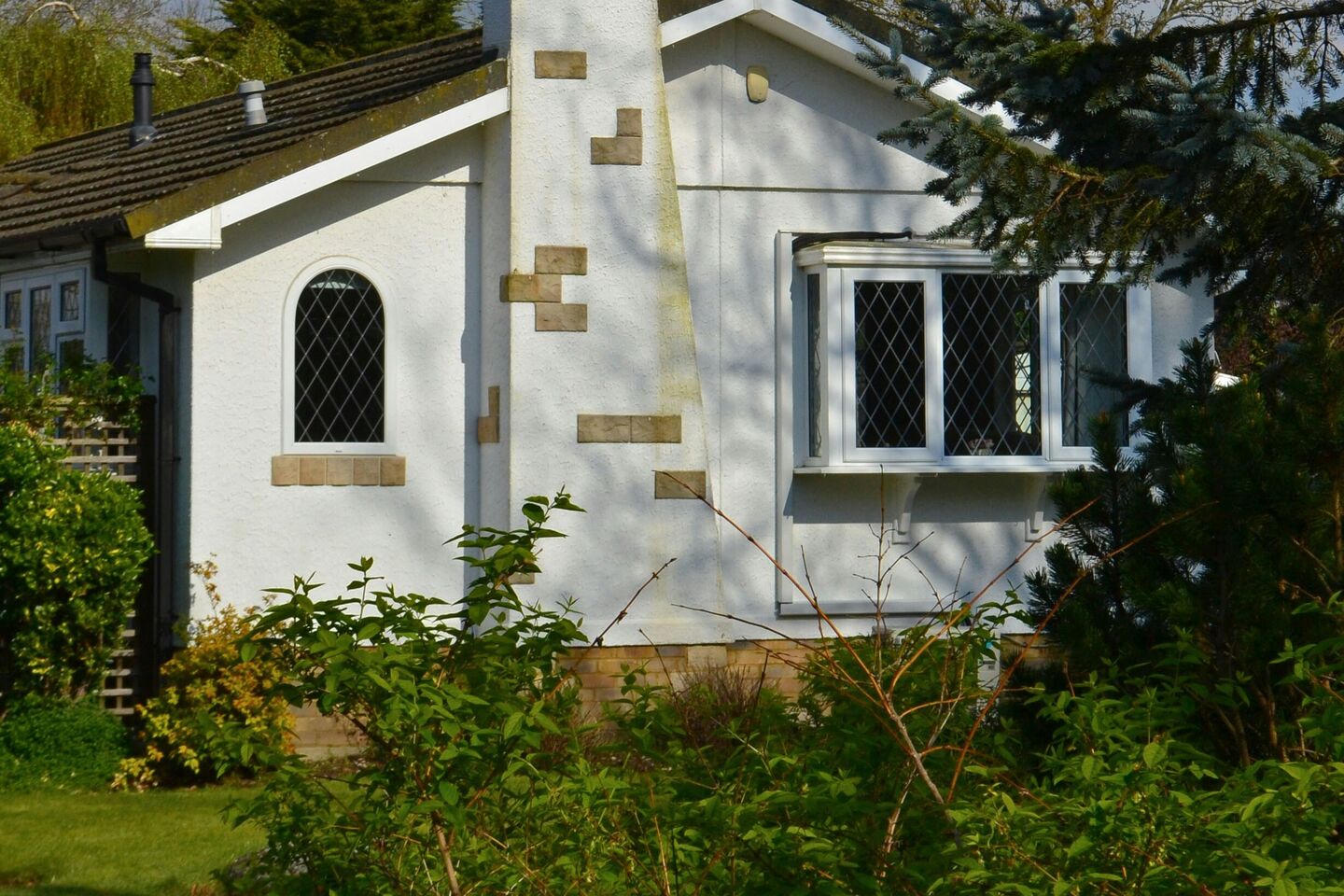 White stucco cottage with a stone chimney and diamond-pane windows