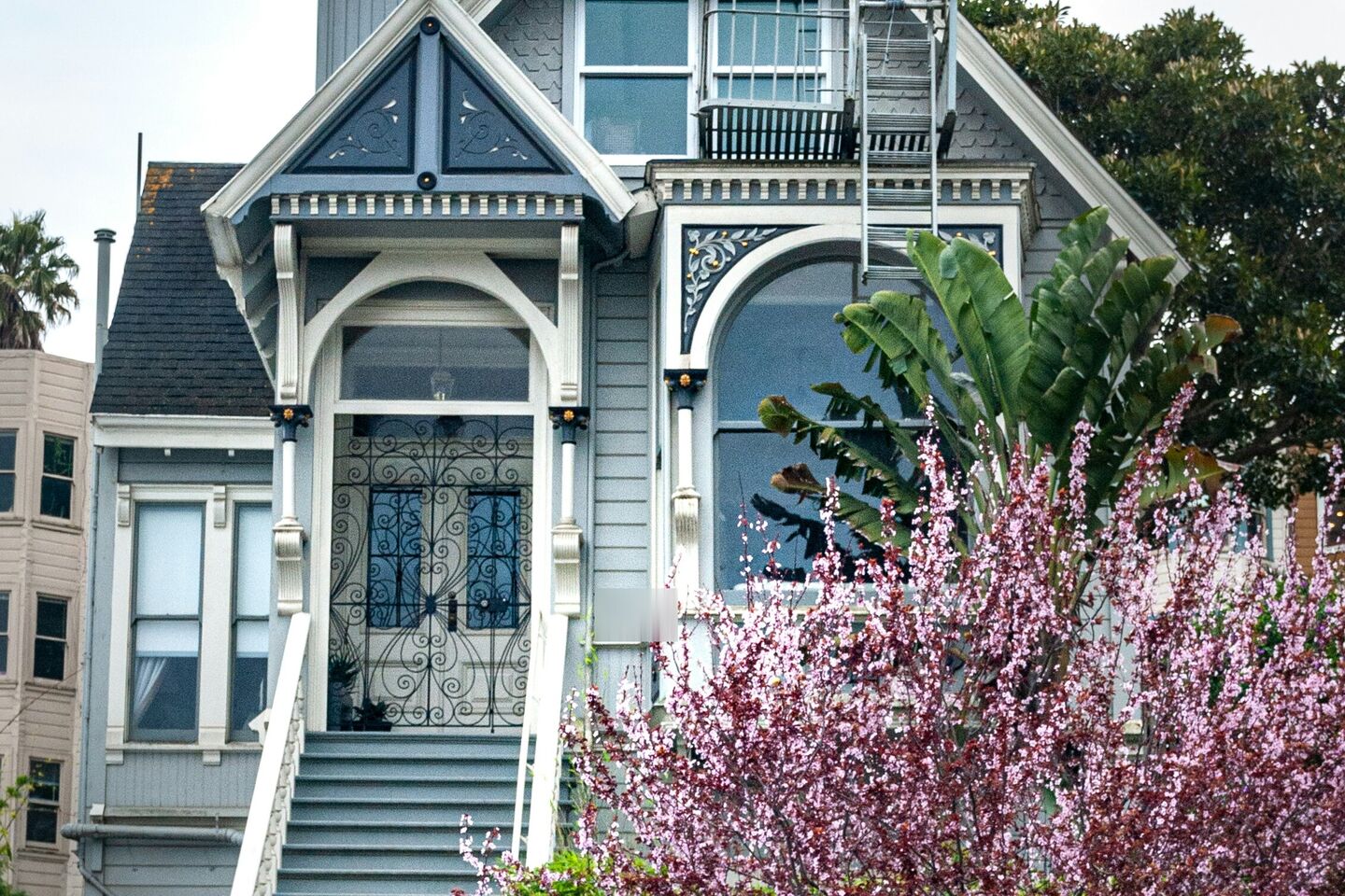 Gray-blue Victorian house with an arched front door and a flowering tree
